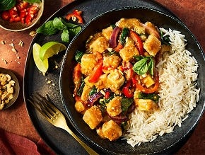 Quorn Pieces in a Massaman curry sauce with chopped peppers and onion served with white rice in a black bowl with lime garnish.