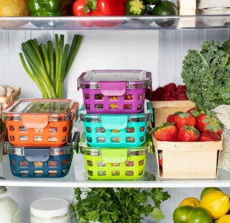 A refrigerator shelf with several colorful food containers, brussels sprouts, mushrooms, kale, strawberries, and other fresh produce.